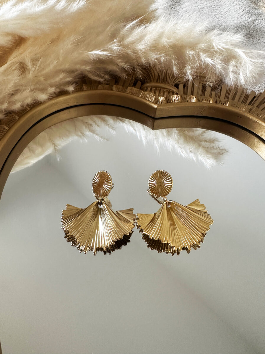 Boucles d'oreilles Morgane dorées en forme d'éventail plissé, posées sur un miroir doré.