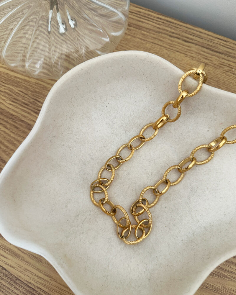 Le collier Carméla est le bijou intemporel qui traverse les saisons sans jamais perdre de son éclat. Ses maillons dorés texturés en acier inoxydable lui donnent une allure à la fois moderne et classique, idéale pour toutes celles qui aiment les pièces fortes et élégantes. Grâce à son design chic et minimaliste, Carméla se porte avec absolument tout ! Matière : acier inoxydable Longueur : 20 cm Fermoir toggle pratique et stylé