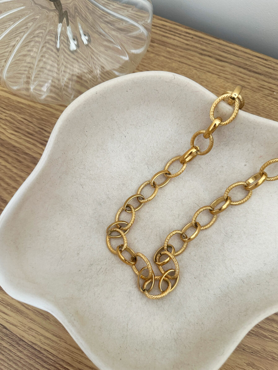 Le collier Carméla est le bijou intemporel qui traverse les saisons sans jamais perdre de son éclat. Ses maillons dorés texturés en acier inoxydable lui donnent une allure à la fois moderne et classique, idéale pour toutes celles qui aiment les pièces fortes et élégantes. Grâce à son design chic et minimaliste, Carméla se porte avec absolument tout ! Matière : acier inoxydable Longueur : 20 cm Fermoir toggle pratique et stylé